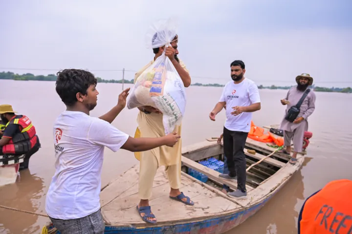 Relief workers handing food supplies to a person in a boat